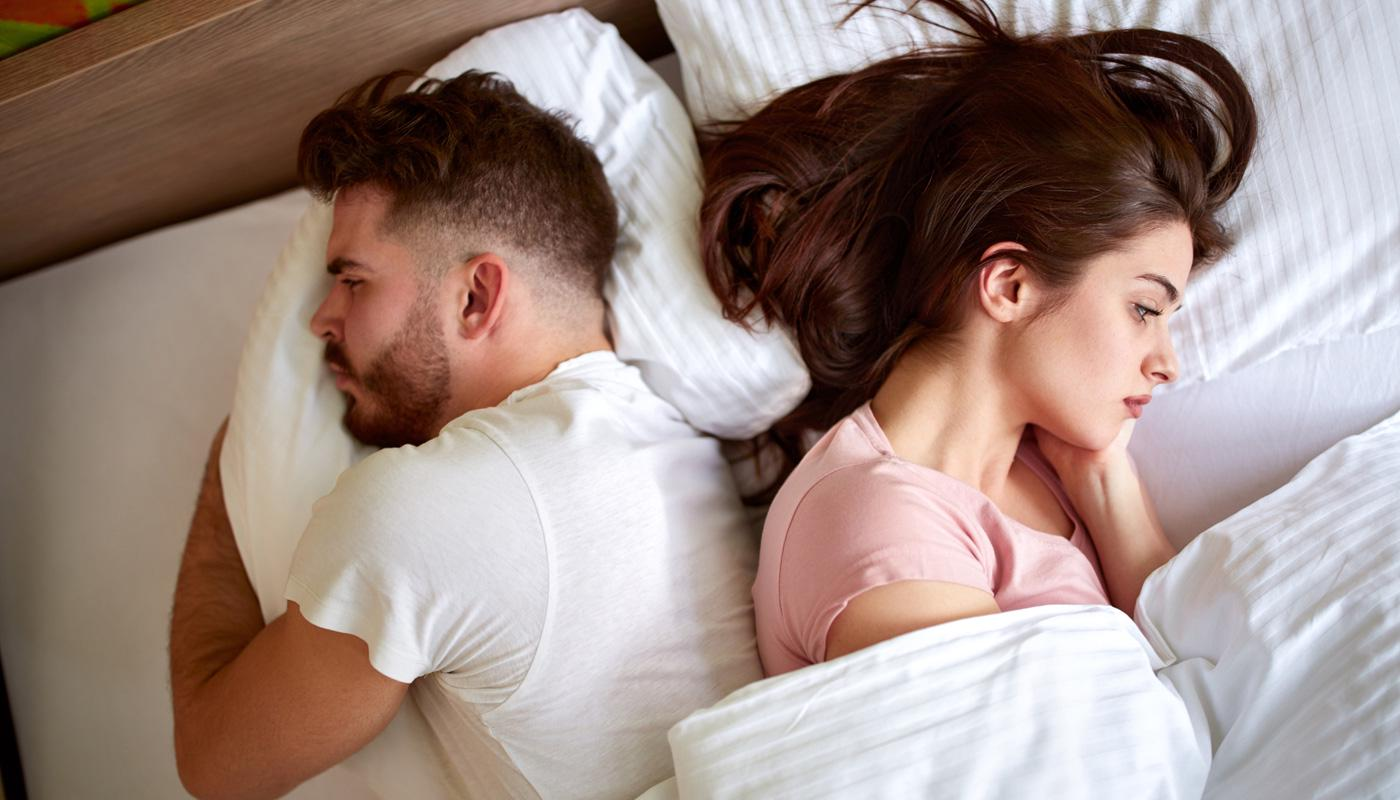 Casal de costas na cama, refletindo dificuldade no relacionamento